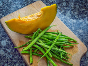 Pumpkin and green beans ready to be chopped on a wooden board